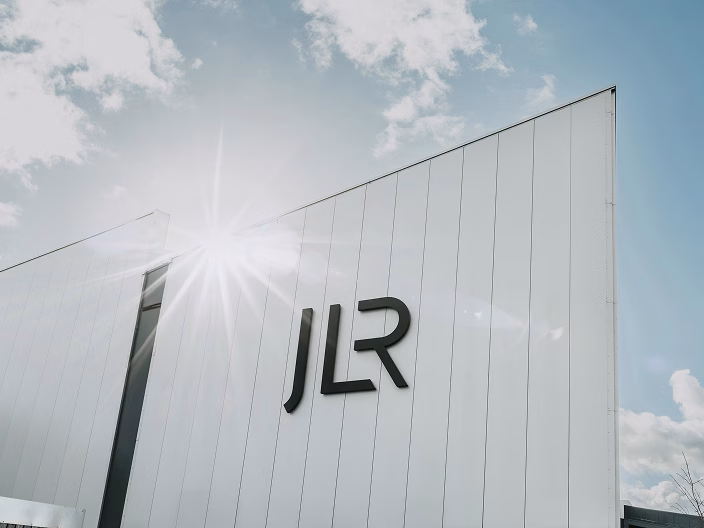 Modern white building exterior with JLR logo under a bright sunny sky representing the luxury car rental UK service powered by Jaguar Land Rover.