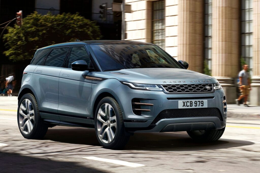 Modern silver Range Rover SUV driving on a city street past a building with tall columns