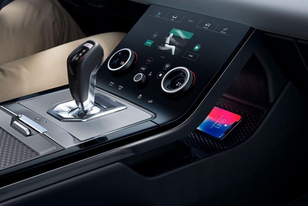 Close-up of a modern car interior showing gear shift lever and touchscreen climate control panel with wireless phone charging area