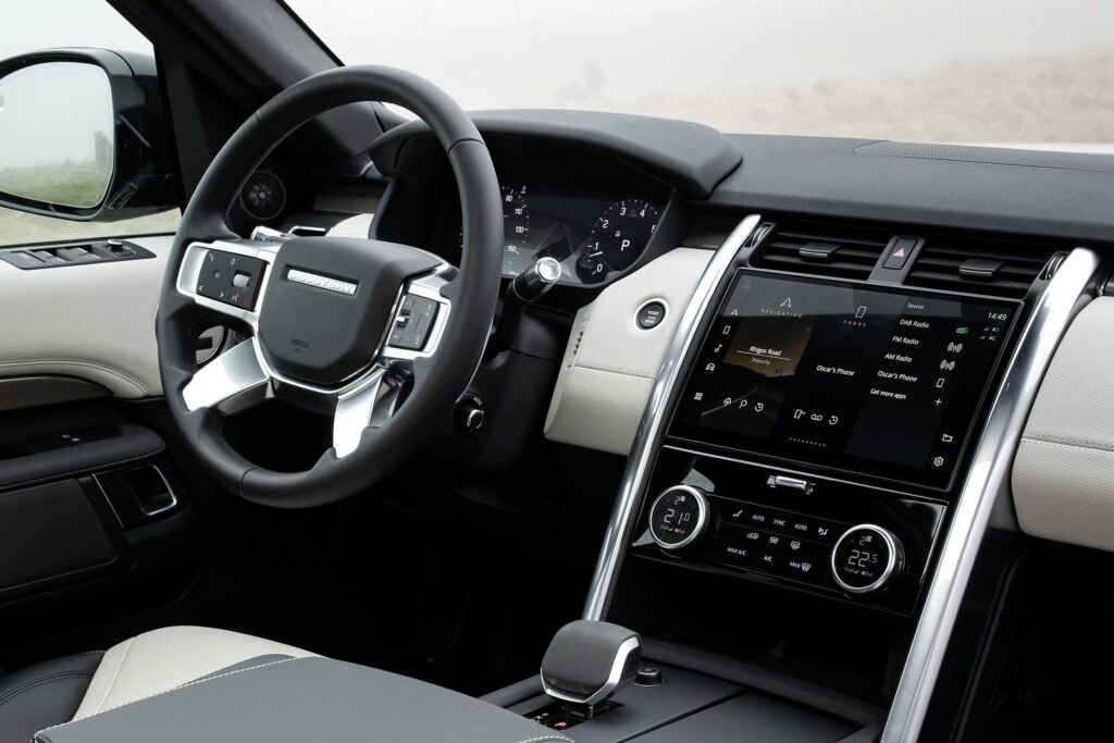 Modern Land Rover Discovery interior showing steering wheel, dashboard, touchscreen and climate controls