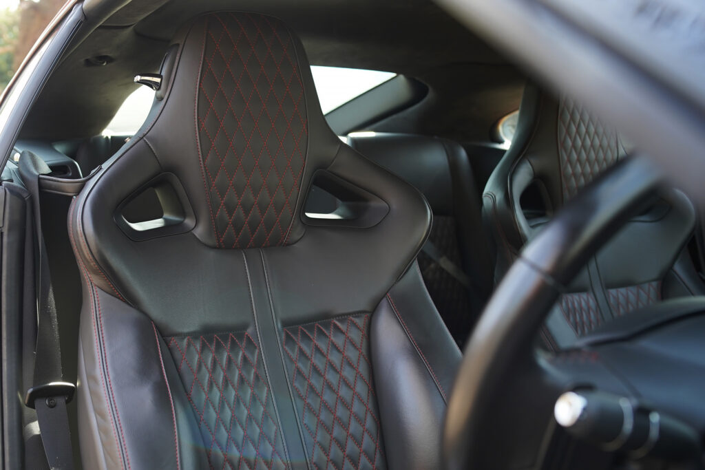 Close-up of luxury black leather car seats with red diamond stitching and sporty design inside a vehicle