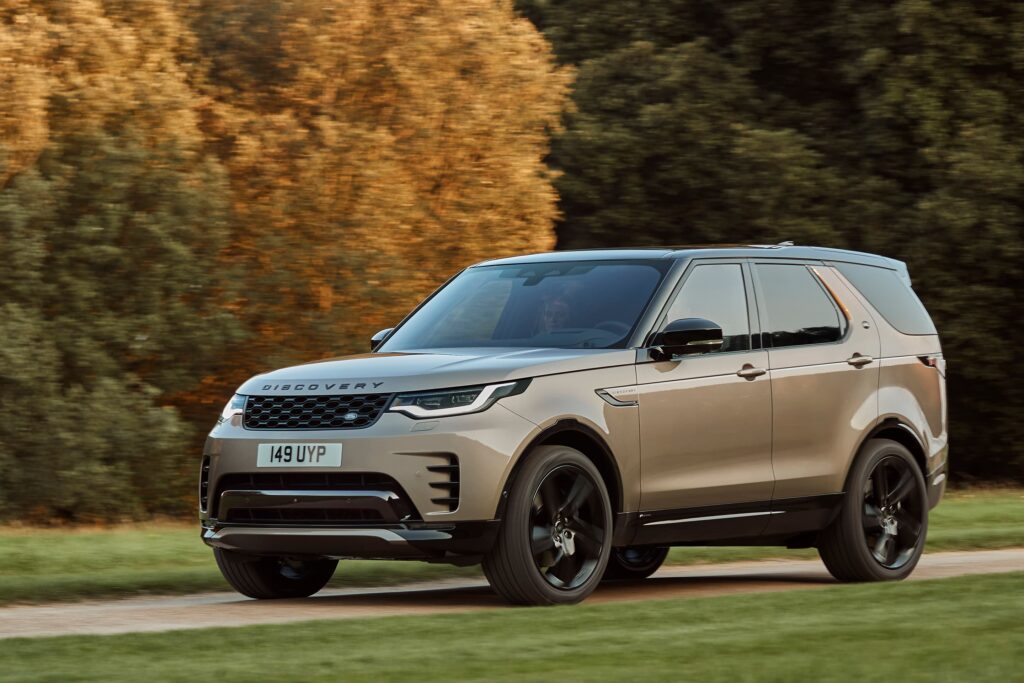 A beige Land Rover Discovery SUV driving on a rural road with autumn trees in the background, illustrating luxury car rental in London.