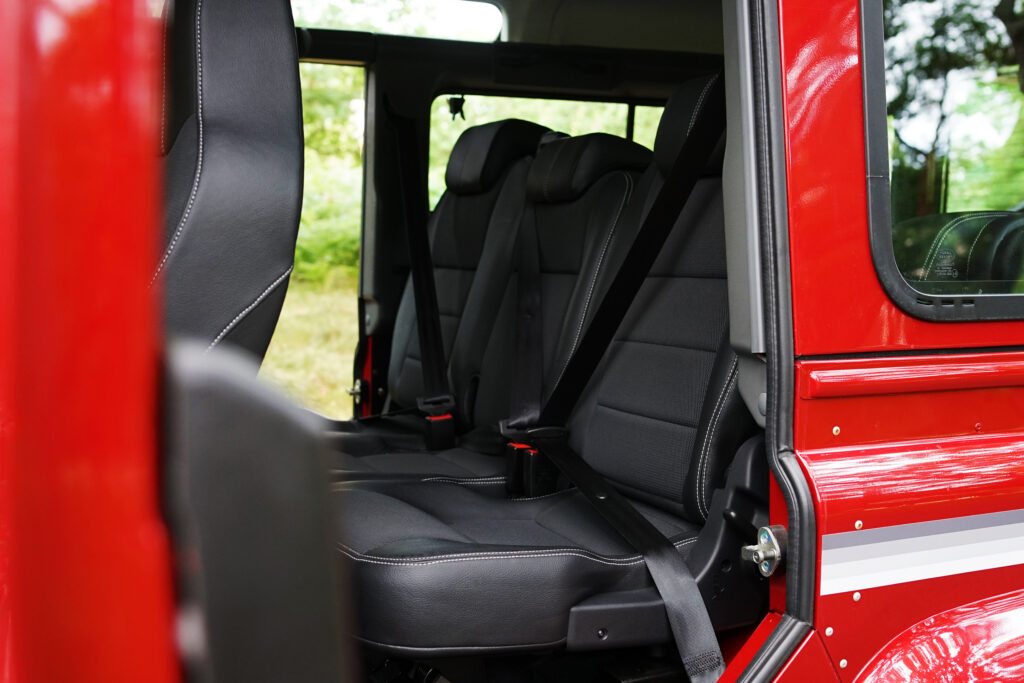 Black leather rear seats with seatbelts inside a red car door opened to show seating area