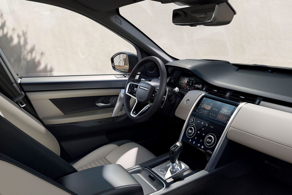 Interior of a luxury car showing black and beige seats, steering wheel, and digital dashboard with climate control and media display