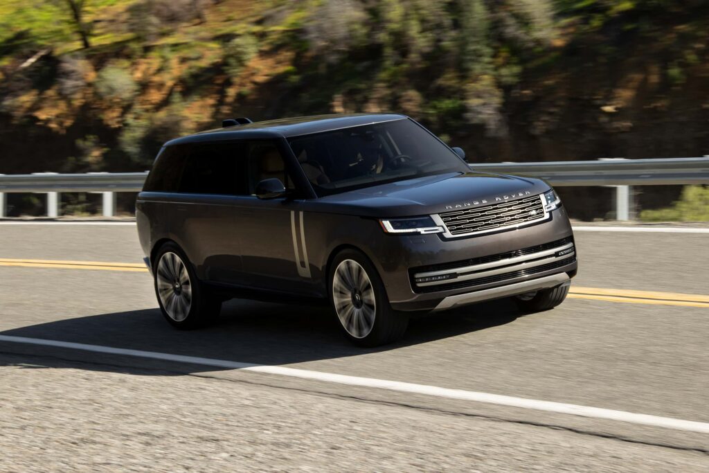 Dark coloured Range Rover SUV driving along a winding mountain road with guardrails and trees in the background