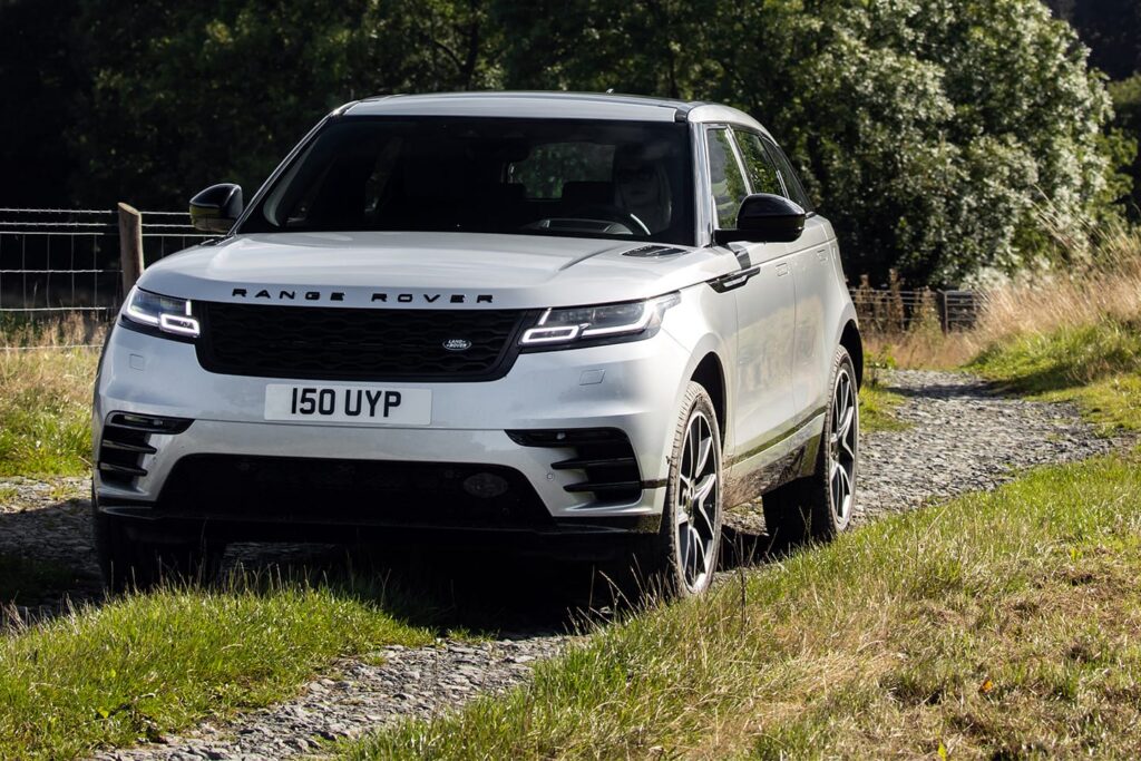 White Range Rover SUV driving on a rural gravel track surrounded by green grass and trees on a sunny day