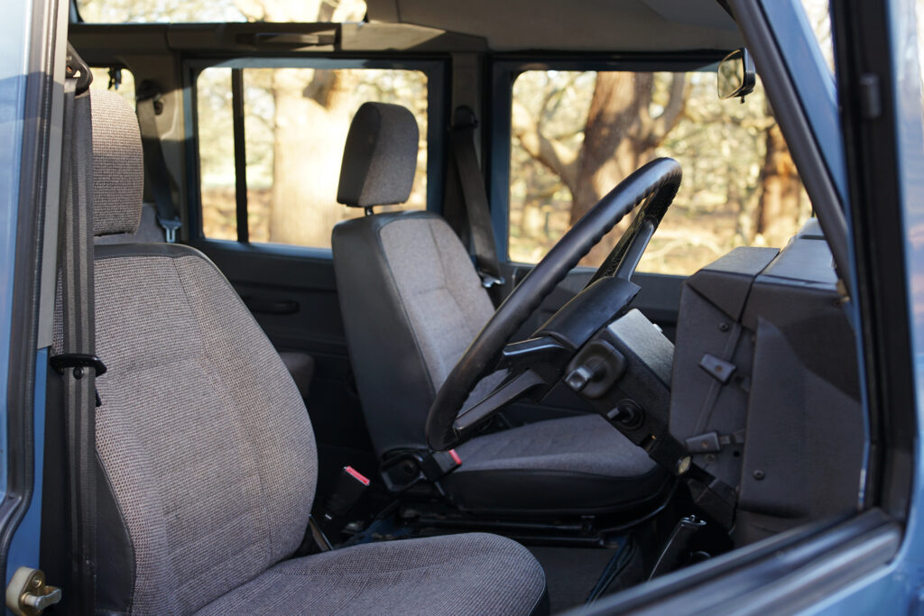 Classic vehicle interior showing the steering wheel and fabric seats against the window view