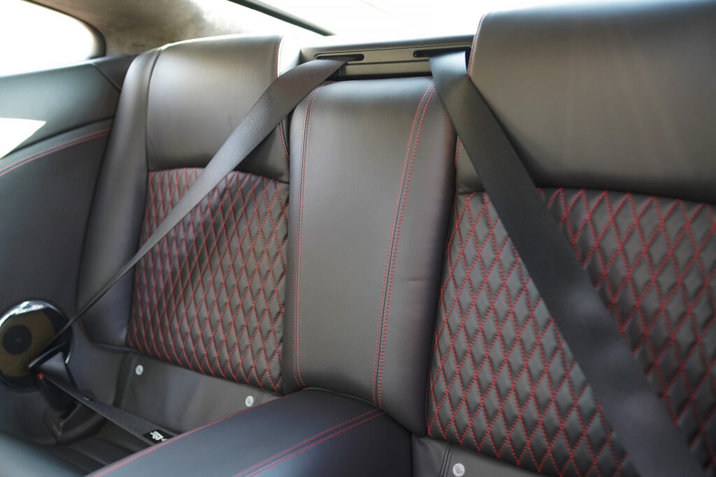Rear black leather car seat featuring red diamond stitching with seat belts fastened
