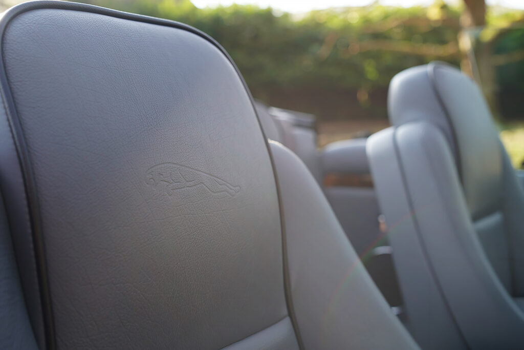 Close-up of a grey leather Jaguar car seat with an embossed logo visible on the headrest