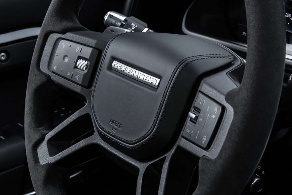 Close-up of a Land Rover Defender steering wheel showing its black suede finish and integrated control buttons