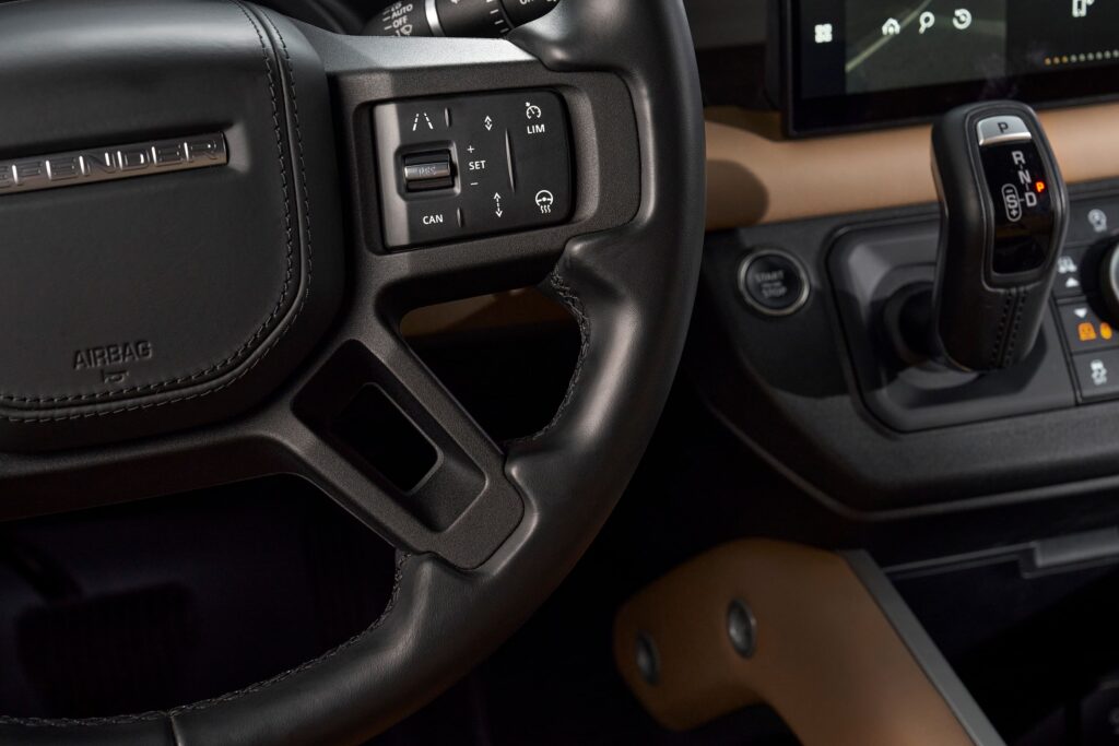 Close-up of Land Rover Defender steering wheel controls and gear lever in leather and tan interior