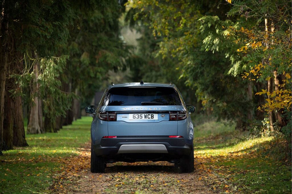 Rear view of a blue Land Rover Discovery Sport parked on a leafy forest path surrounded by tall trees