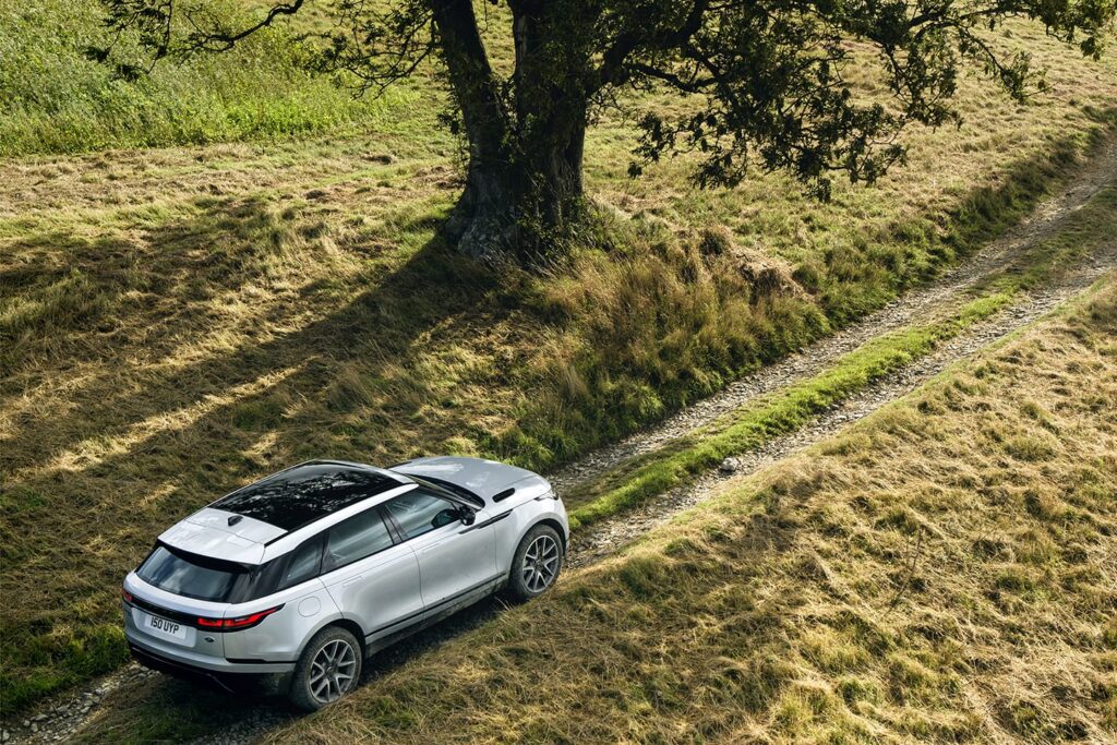 Silver SUV driving on a narrow gravel track beside a large tree in a grassy countryside, illustrating off-road capability.