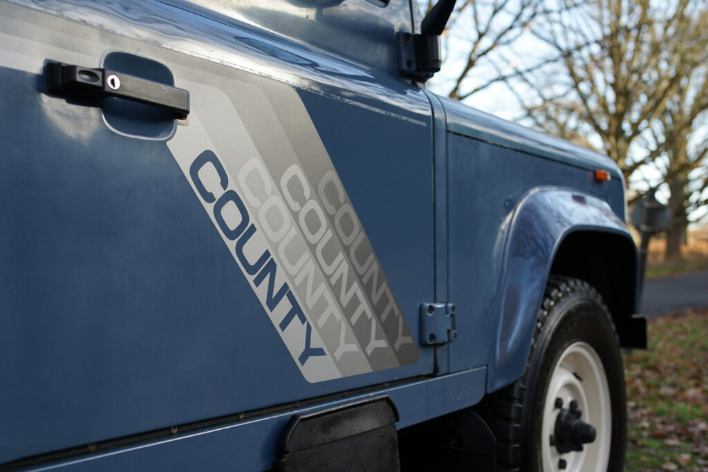 Close-up of a blue Land Rover door featuring the classic 'County' decal in shades of grey and white