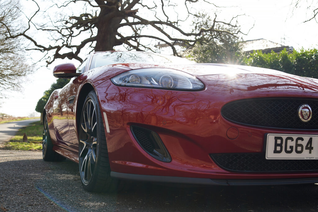 Close-up view of a red Jaguar sports car front side showing detailed headlight, wheel, and grille.