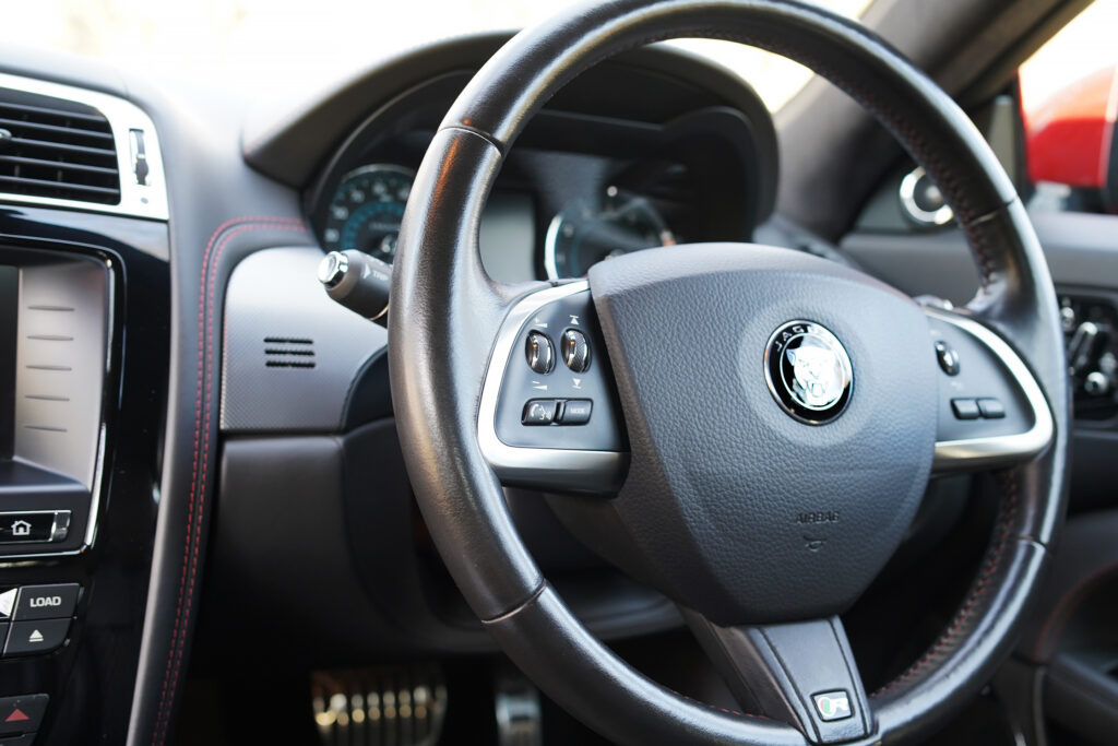 Close-up of a Jaguar car's leather-wrapped steering wheel with control buttons and dashboard indicators
