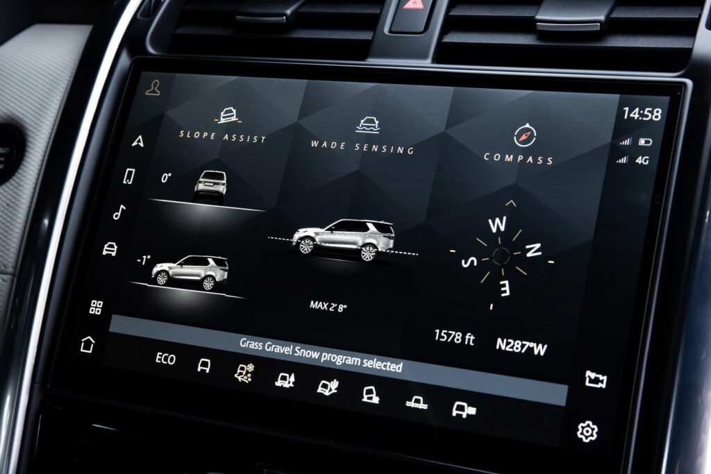 Vehicle touchscreen displaying vehicle terrain options including slope assist, wade sensing, compass, and grass gravel snow mode on a car dashboard.