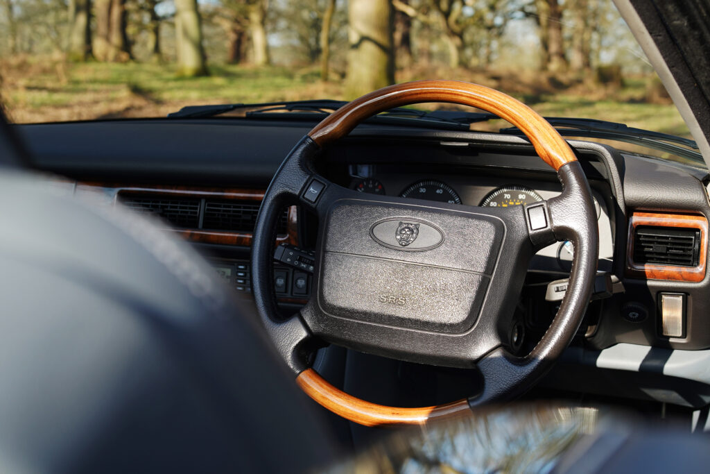Classic Jaguar car steering wheel with wooden trim and dashboard details under natural light.