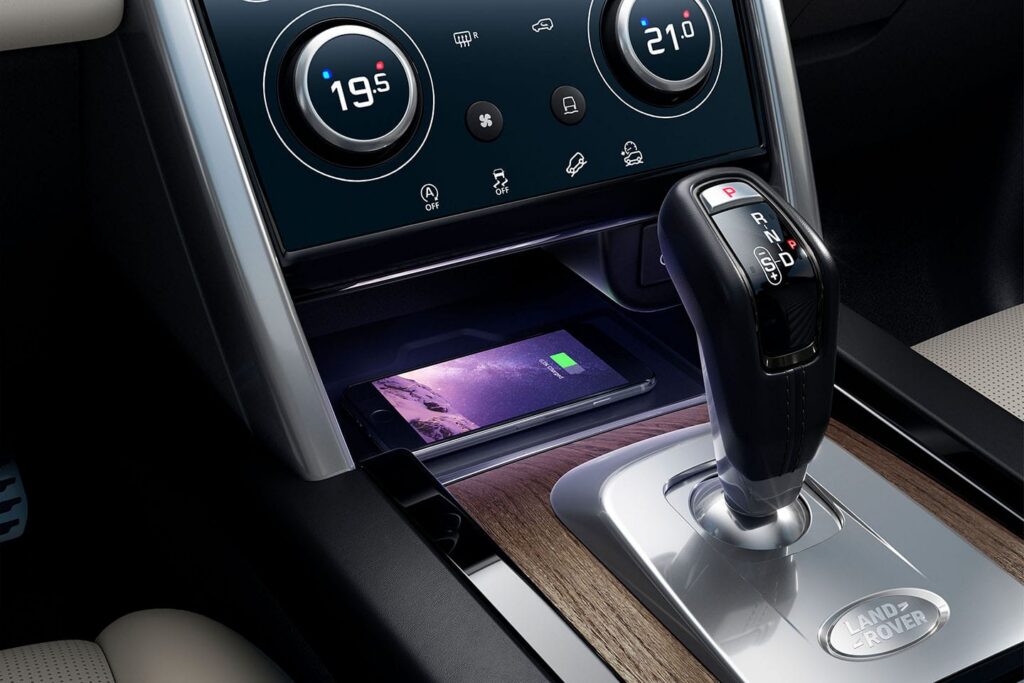 Gear shift and dual-zone climate control panel in a Land Rover car interior with a smartphone wirelessly charging below the dashboard