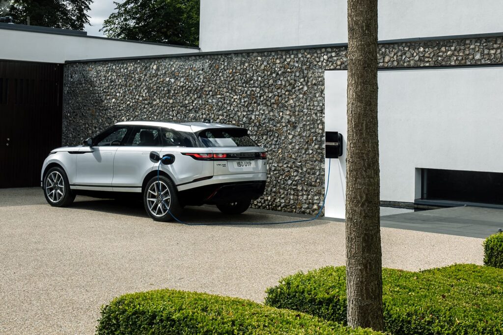 White electric SUV charging at a wall-mounted home charging station in a modern driveway with stone and white walls