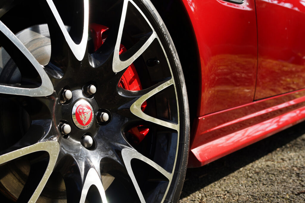 Close-up of a Jaguar car wheel with black and silver rim and red brake caliper on a red car body