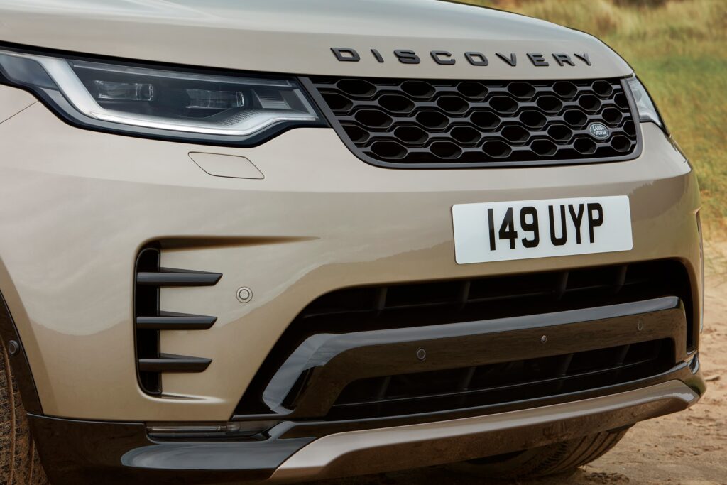 Close-up of a beige Land Rover Discovery front grille and headlight showing the discovery name and UK-style number plate.