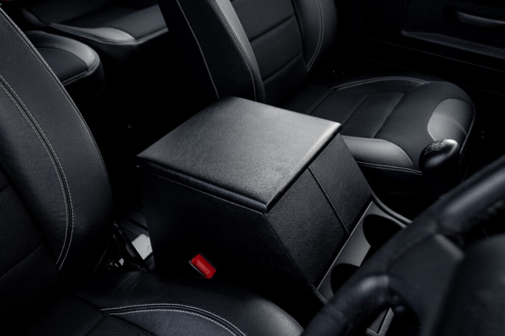 Black leather car seats with contrasting white stitching and a leather armrest in the centre console area, showcasing car interior details.
