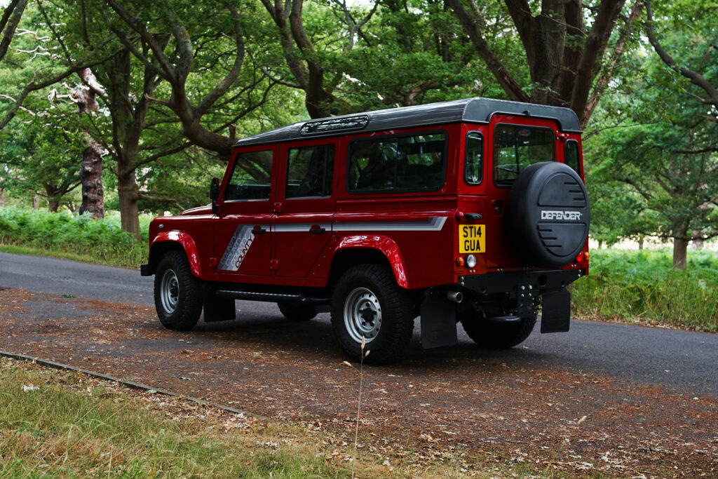 Red Land Rover Defender County classic model parked on a forest road with green trees around