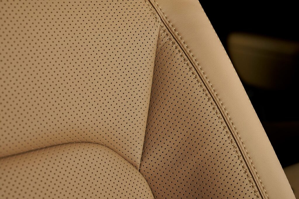 Close-up view of tan perforated leather upholstery on a car seat showing fine stitching and texture detail.