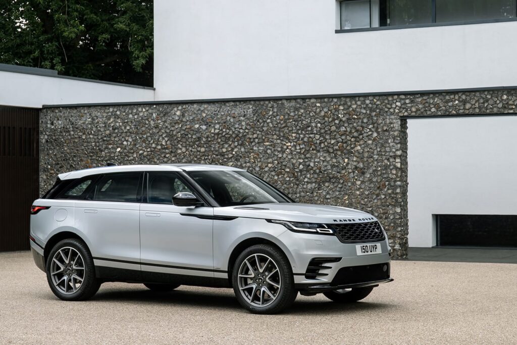 Silver Range Rover Velar SUV parked in front of modern house with flint wall, showcasing stylish exterior design and luxury features.