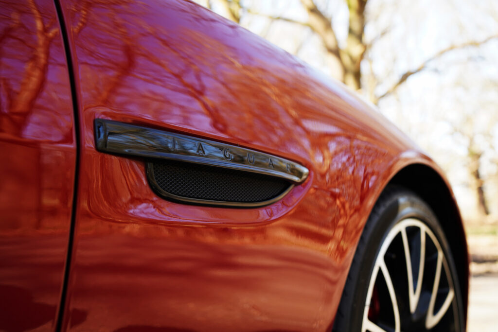 Close-up of a red Jaguar car's side vent and wheel, highlighting the Jaguar badge and glossy finish