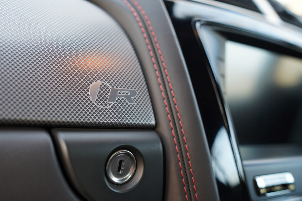 Close-up of a car's interior showing the R logo badge on the dashboard panel with red stitching near the ignition