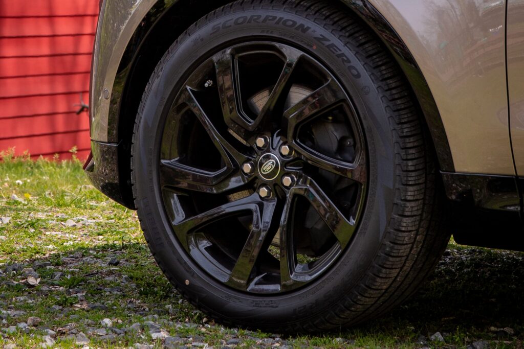 Close-up of a black Land Rover car wheel and tyre on grass and gravel surface