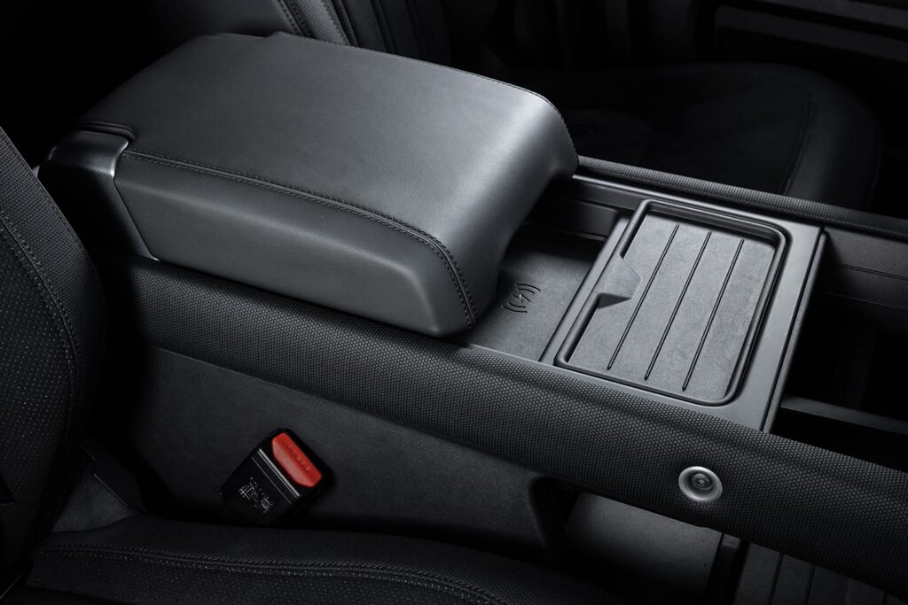 Close-up of a black leather car interior central armrest featuring a wireless charging pad and seatbelt buckle.