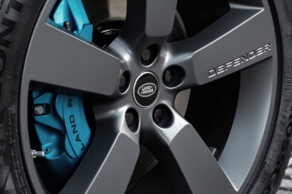 Close-up of a Land Rover Defender alloy wheel with blue brake caliper and visible Land Rover branding, highlighting vehicle detail.