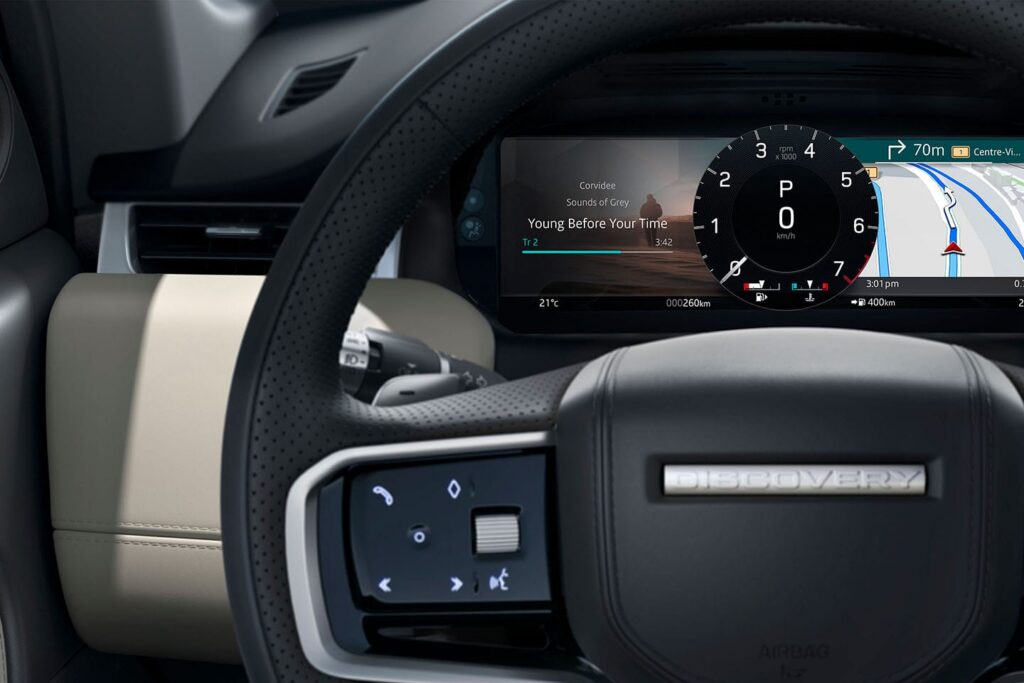 Close-up of a Discovery vehicle steering wheel showing multimedia controls and a digital dashboard displaying navigation and audio information.
