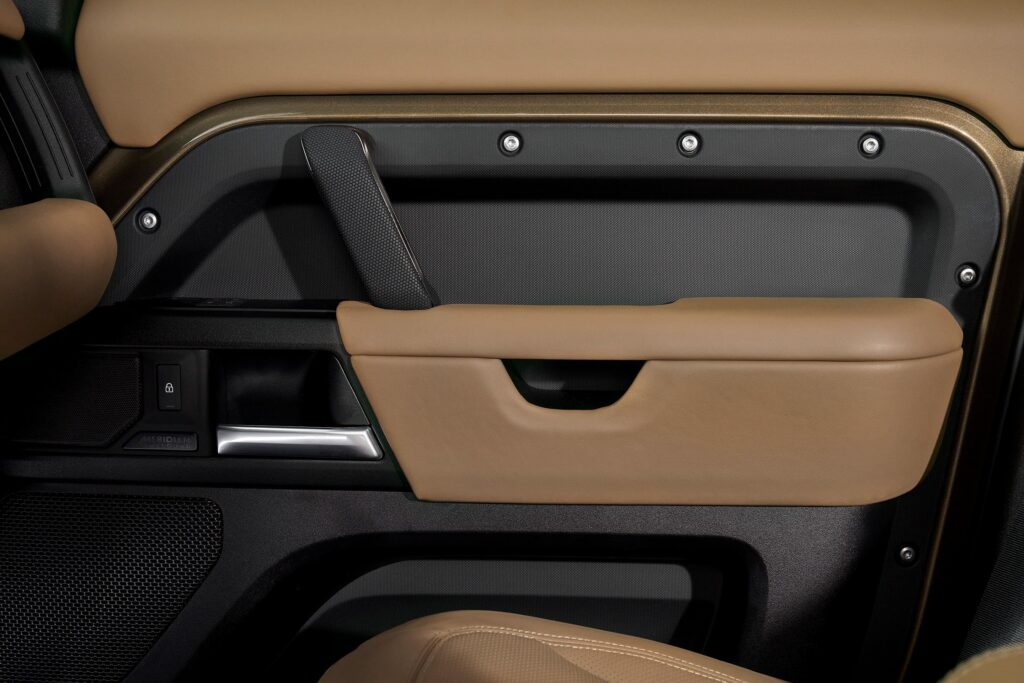Beige and black car door panel showing armrest, door handle, lock switch, and a speaker grille with Meridian branding