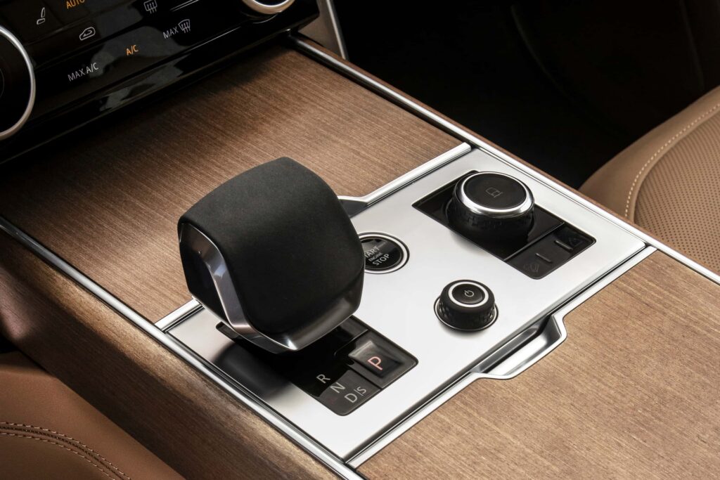 Close-up of a car gear selector and control knobs on wood trim interior panel in a luxury vehicle