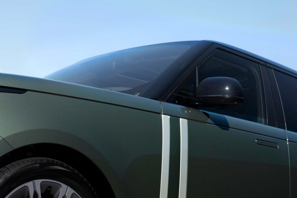 Close-up of a green car's side panel featuring two white vertical stripes, a black side mirror, and alloy wheel under clear sky