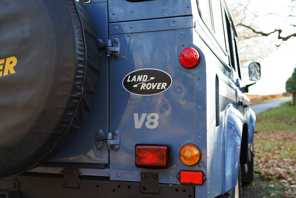 Close-up of the rear section of a blue Land Rover V8 showing badges and rear lights