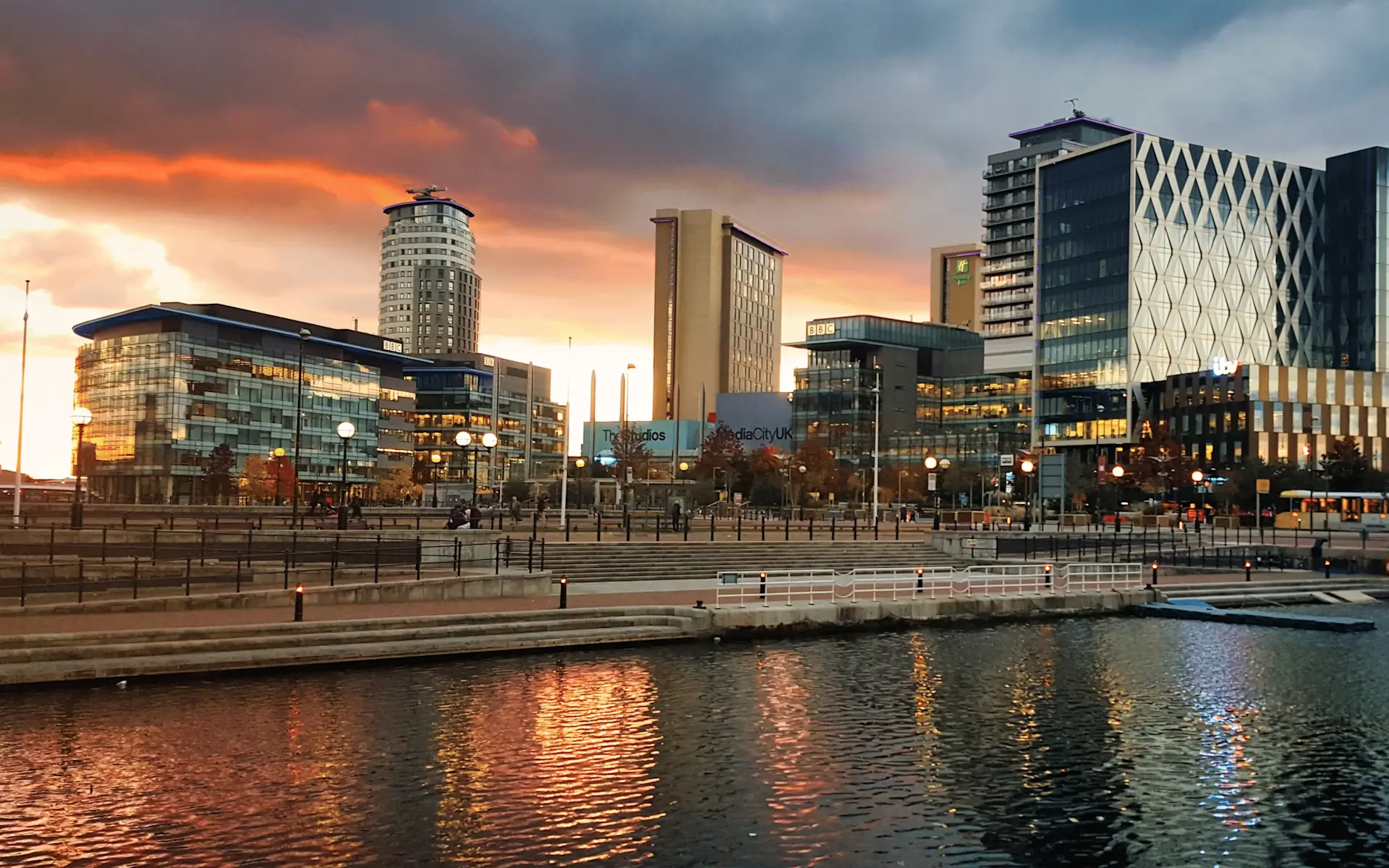 Sunset over Manchester skyline reflecting in water, showing modern buildings including MediaCityUK, illustrating the city environment for luxury car hire Manchester service.