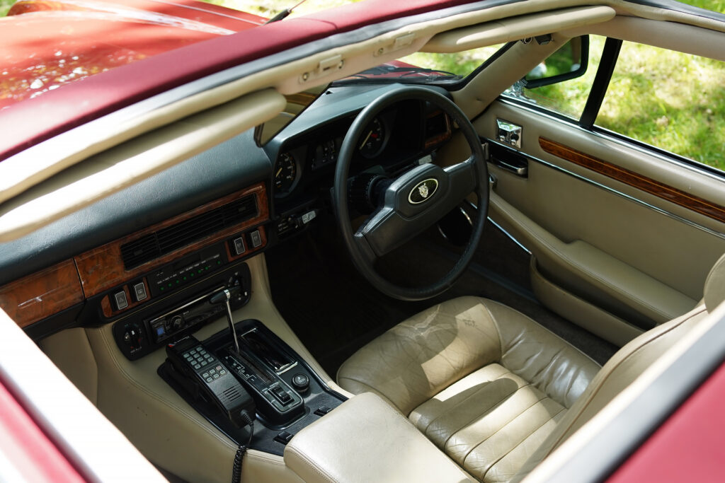 Interior of a classic Jaguar car with tan leather seats, wooden dashboard trim, and a vintage car phone beside the gear lever.