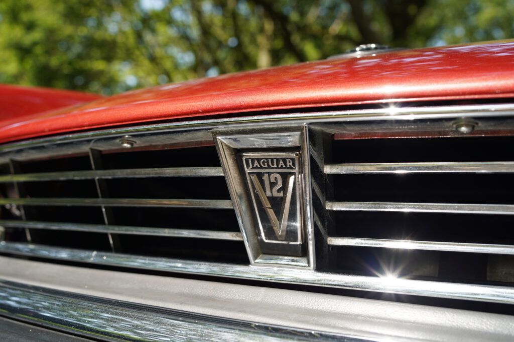 Close-up of the Jaguar 12 V badge on a red classic car grille with sunlight reflections