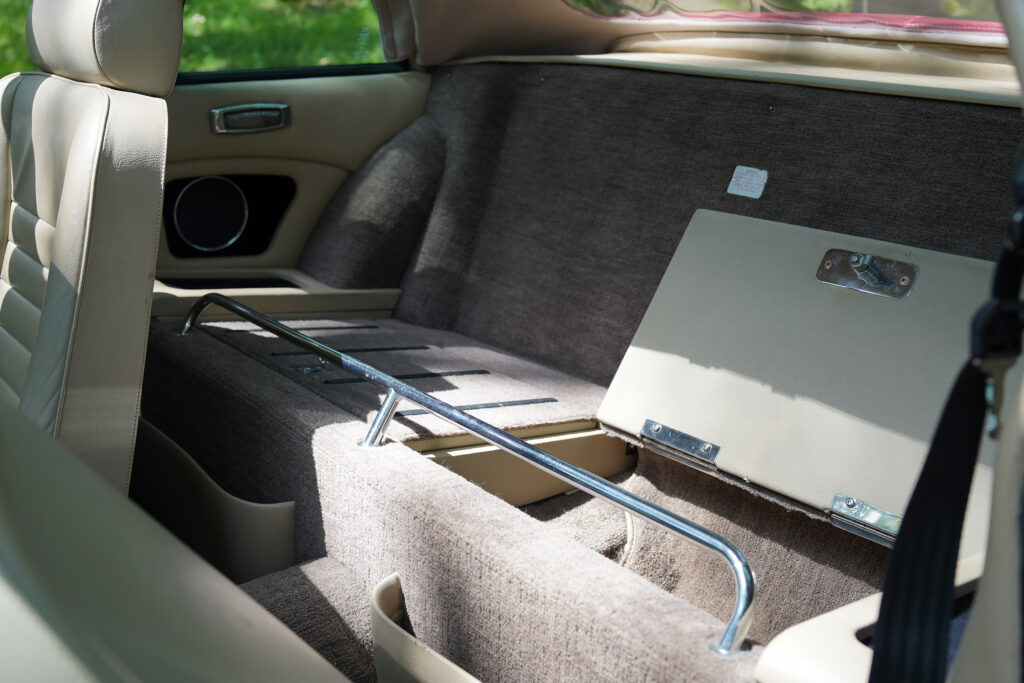 Interior of a classic car showing beige leather seats and a rear storage compartment with a hinged cover open