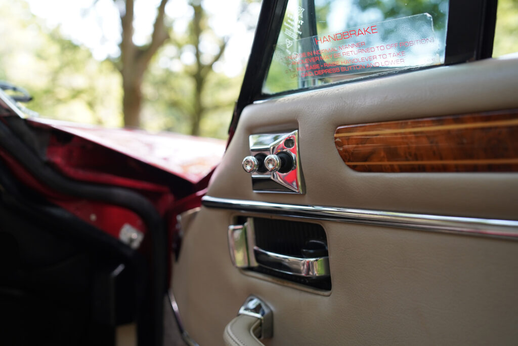 Close-up of a vintage car door interior showing beige leather, chrome handles, and wooden trim, highlighting classic car craftsmanship.