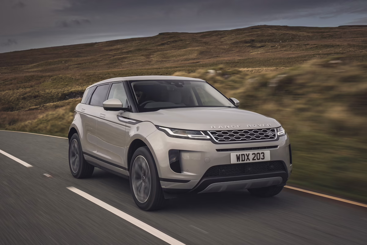 Silver Range Rover Evoque driving along a countryside road with hills in the background